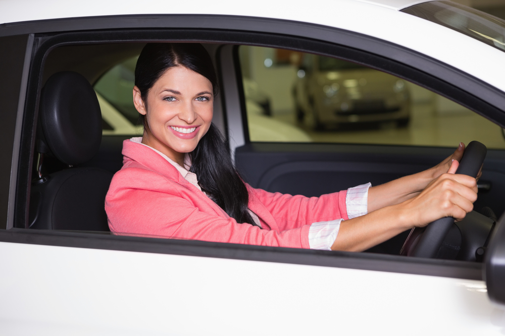 Smiling woman sitting at the wheel of her new car at new car showroom